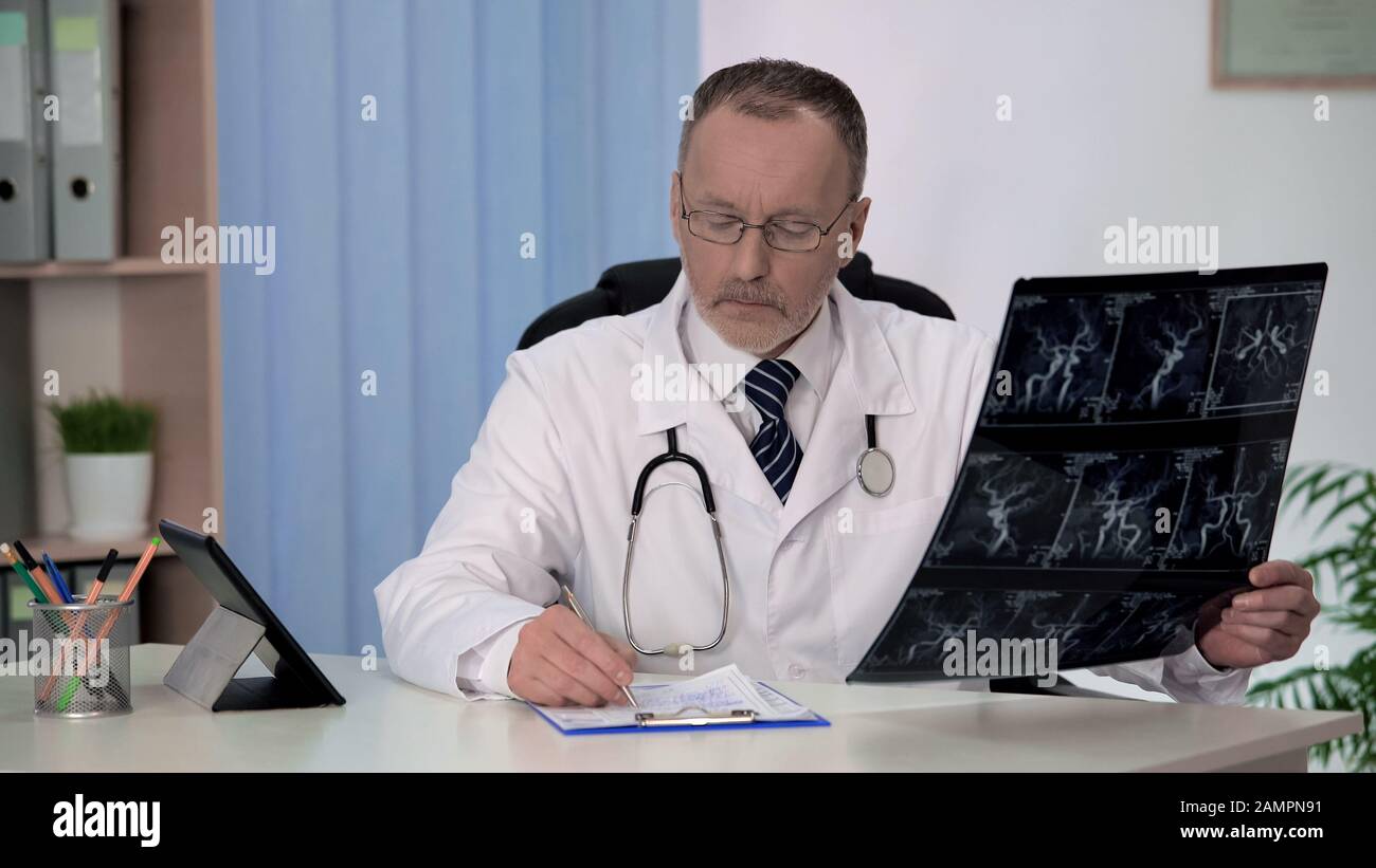 Neurologist checking angiography of blood vessels, writing prescription in form Stock Photo