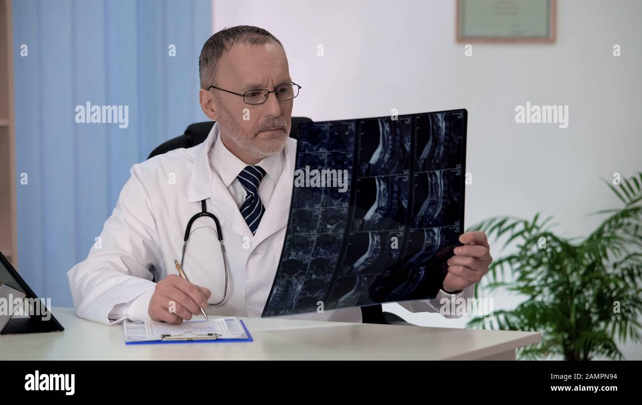 Spinal surgeon examining backbone mri, making notes in patients medical record Stock Photo