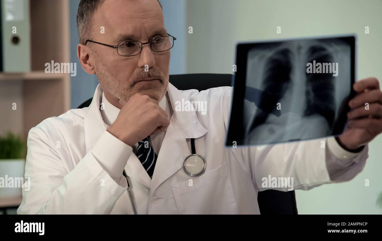 Male pulmonologist scrutinizing chest x-ray, looking for pathology, diagnostics Stock Photo