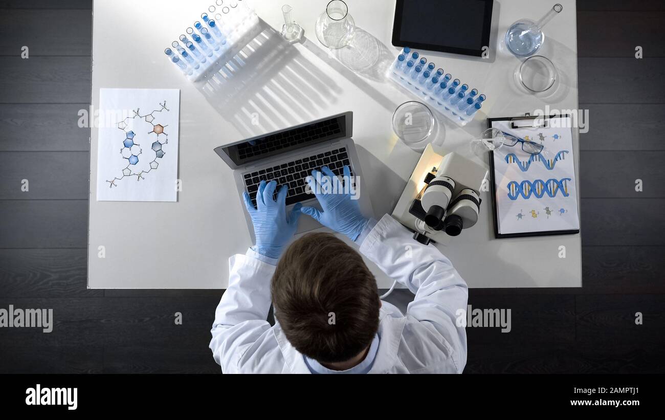 Lab worker viewing samples under microscope and typing results on laptop topview Stock Photo