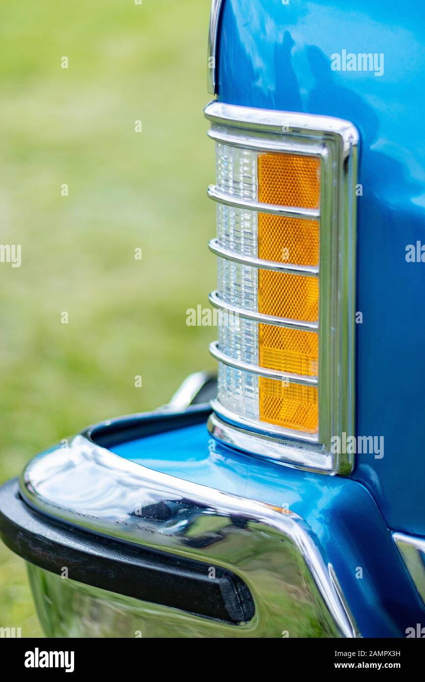 Close-up of a vintage blue car's rear orange and chrome tail light against a blurred green background Stock Photo