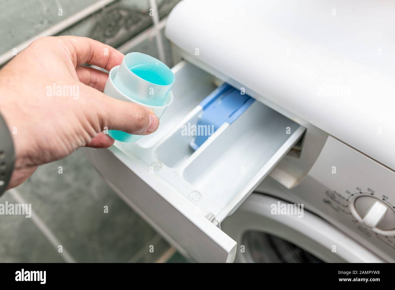 Male hand pouring laundry detergent into washing machine before doing the laundry Stock Photo