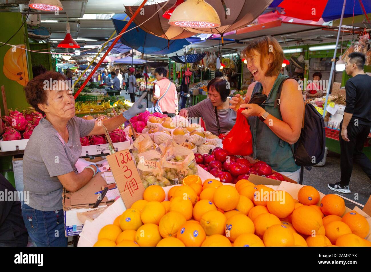 Hong Kong tourist - a woman tourist buying fruit from a market stall, Bowring street market, Kowloon Hong Kong Asia - example of Hong Kong travel Stock Photo