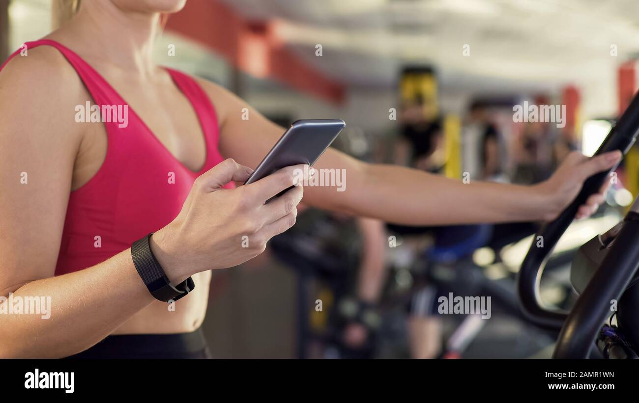 Female with wristband riding stationary bike and monitoring distance on phone Stock Photo