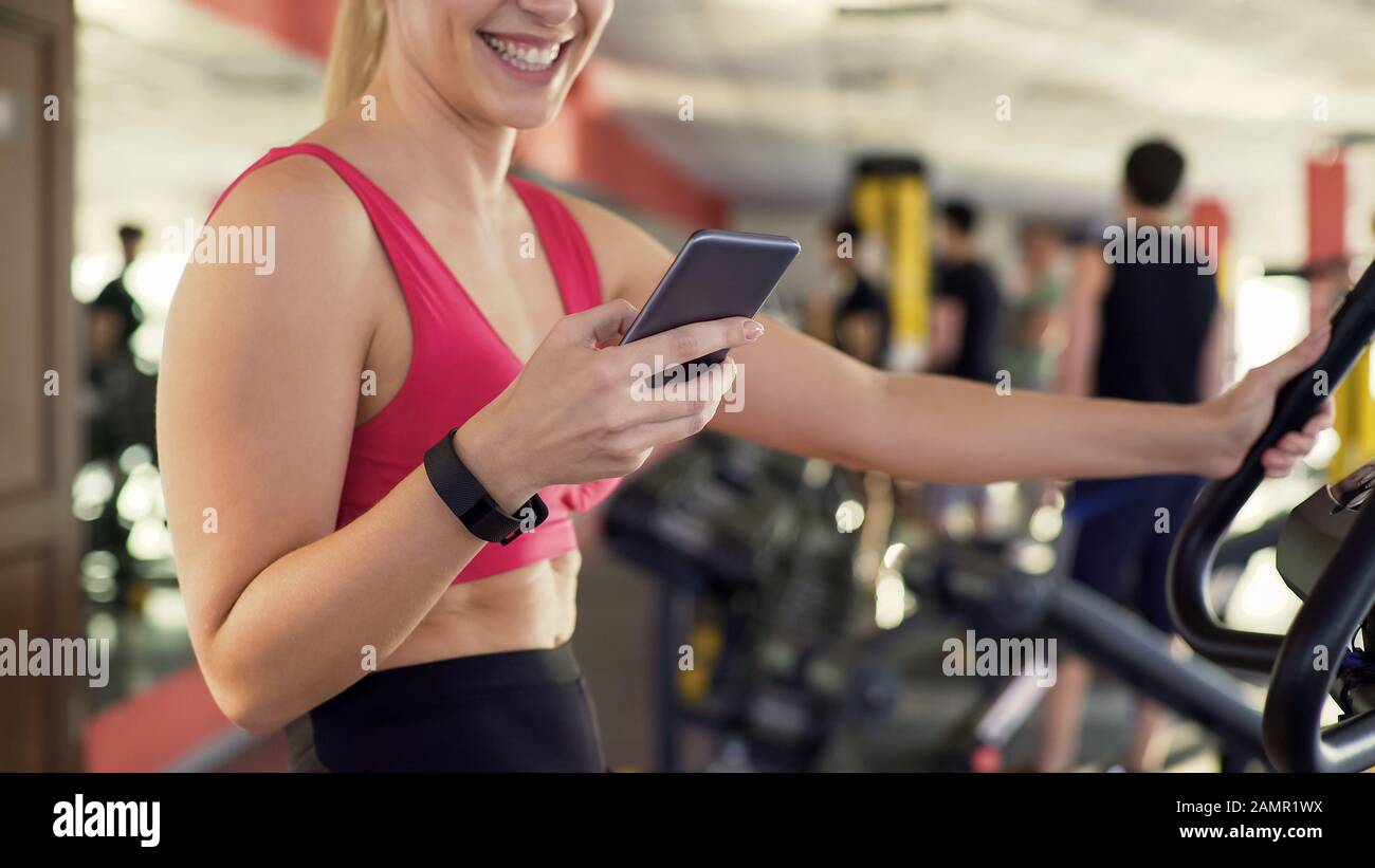 Athlete with fitness bracelet riding exercise bike and chatting on cellphone Stock Photo