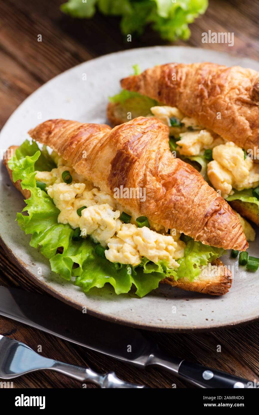 Croissant filled with scrambled eggs, cheese and green lettuce leaf salad. Tasty breakfast food, continental breakfast concept Stock Photo