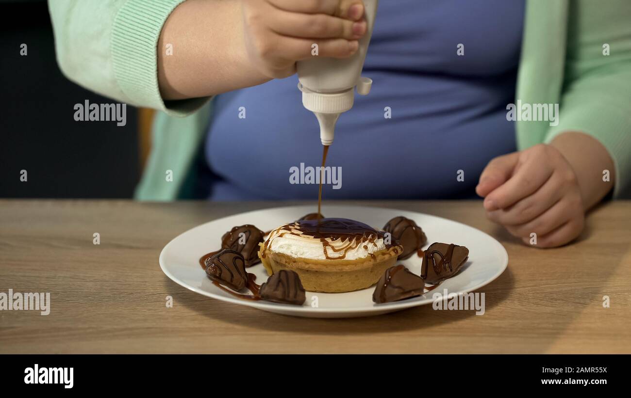 Obese female adding too much chocolate to pastry, overeating sugar and sweets Stock Photo