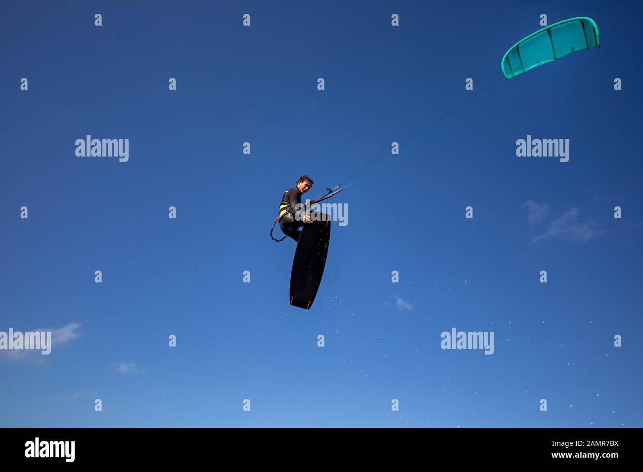 Sporty Kitesurfer having fun in the air during a jump. Updraft with board grab. Stock Photo