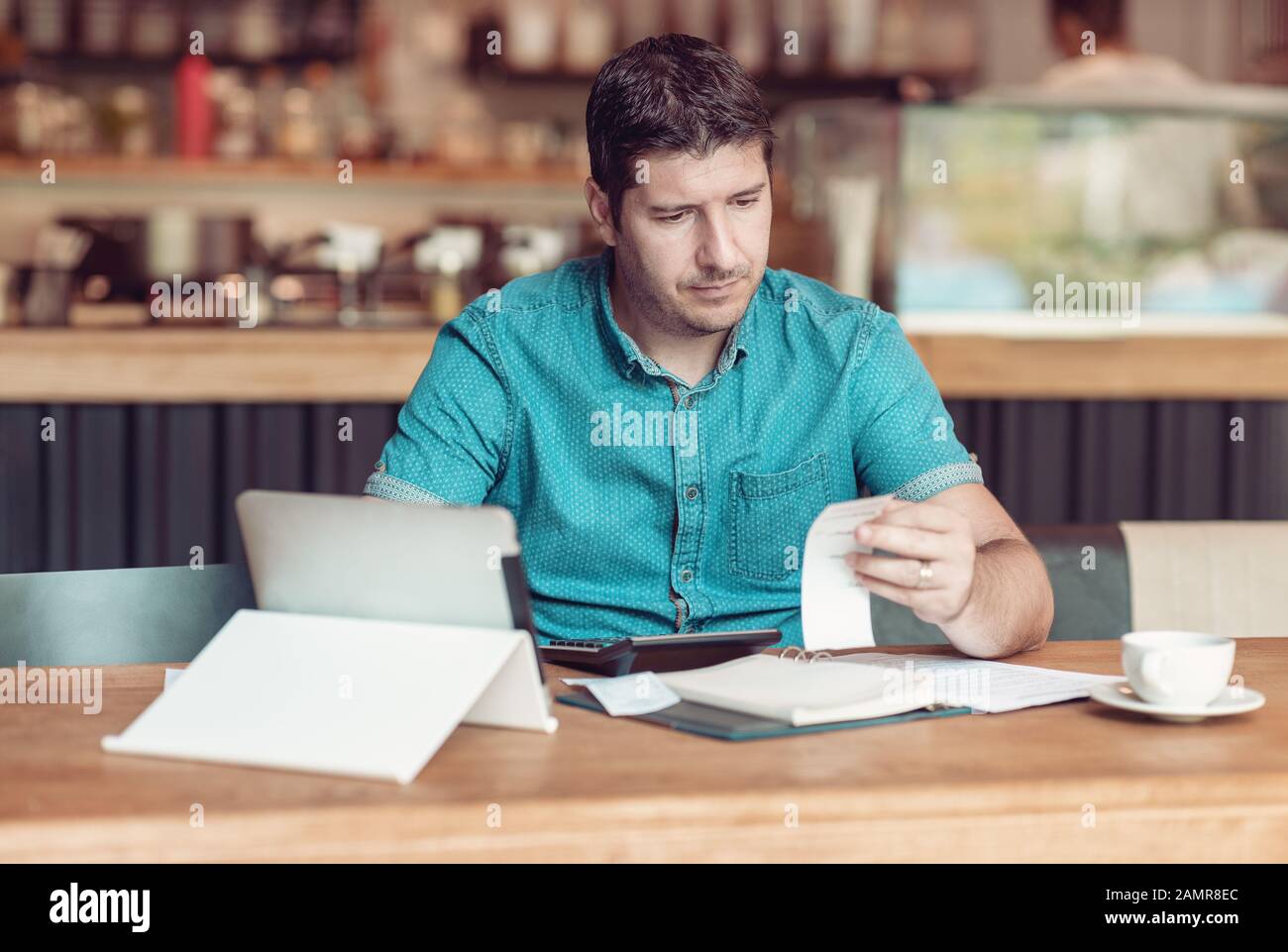 Entrepreneur managing his small business - Businessman looking overwhelmed - Young coffee shop owner going through paperwork Stock Photo