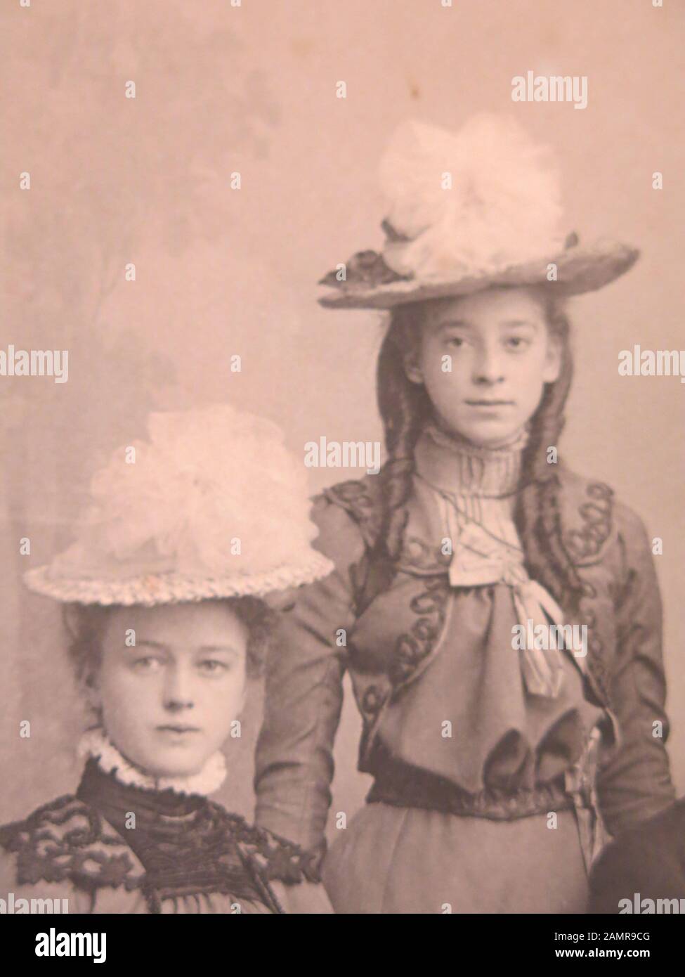 Sepia portrait of two young women in very ornate hats and costumes, one with long ringlets; late nineteenth century. Stock Photo