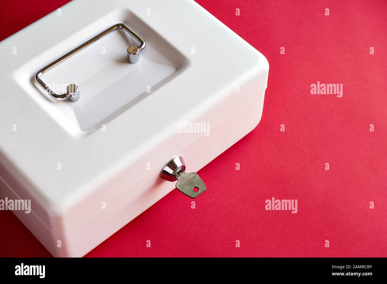 Close up of small white closed cashbox or money box with key in lock on dark pink background with copy space. Stock Photo