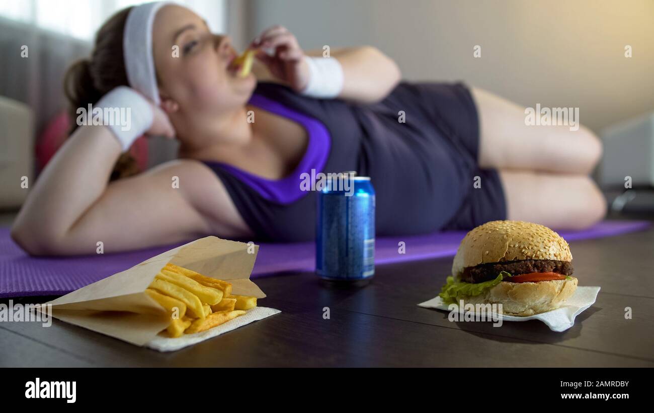 Fat lazy girl in sportswear eating junk food instead of training