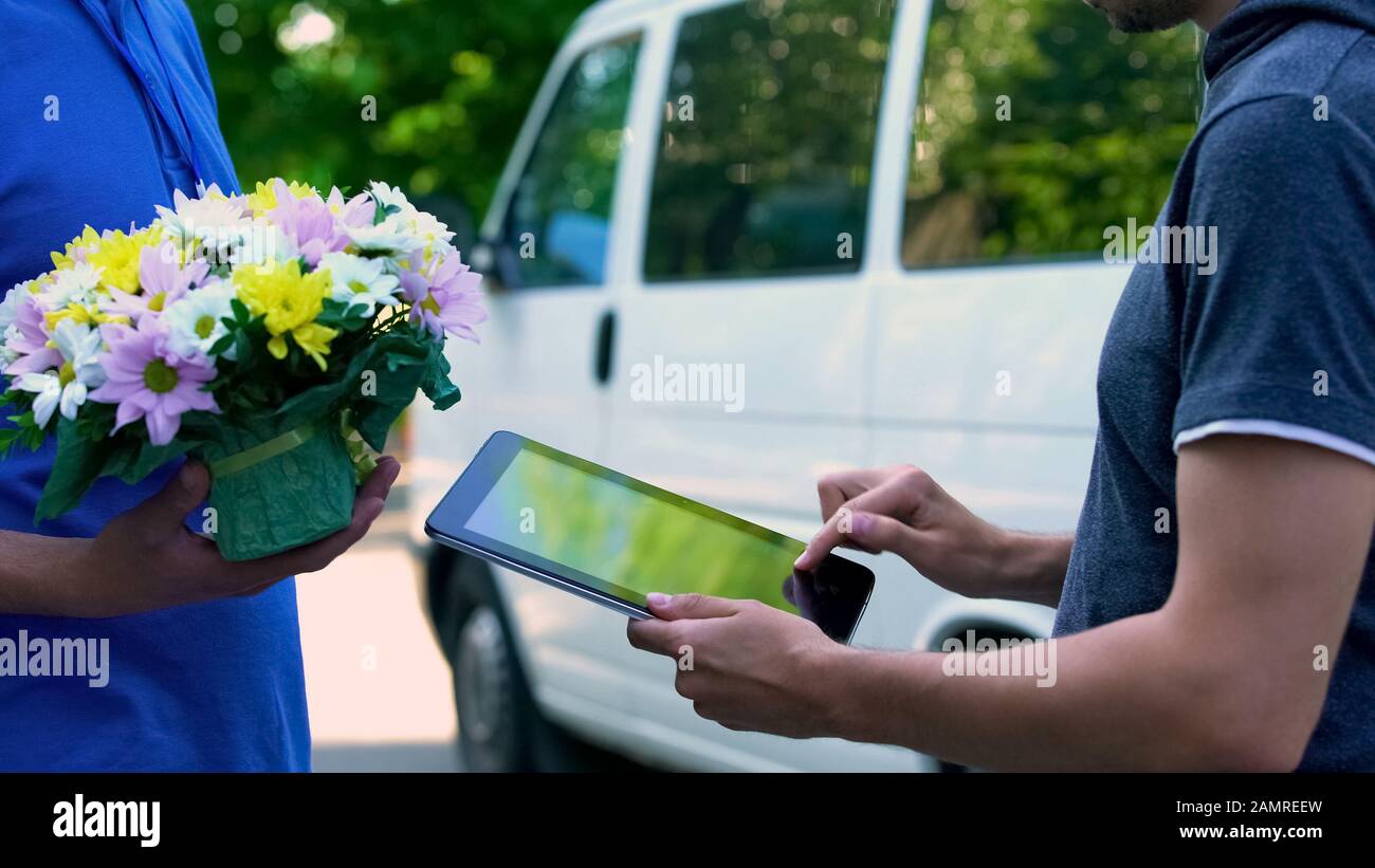 Man appending signature on tablet and receiving flower present from delivery man Stock Photo