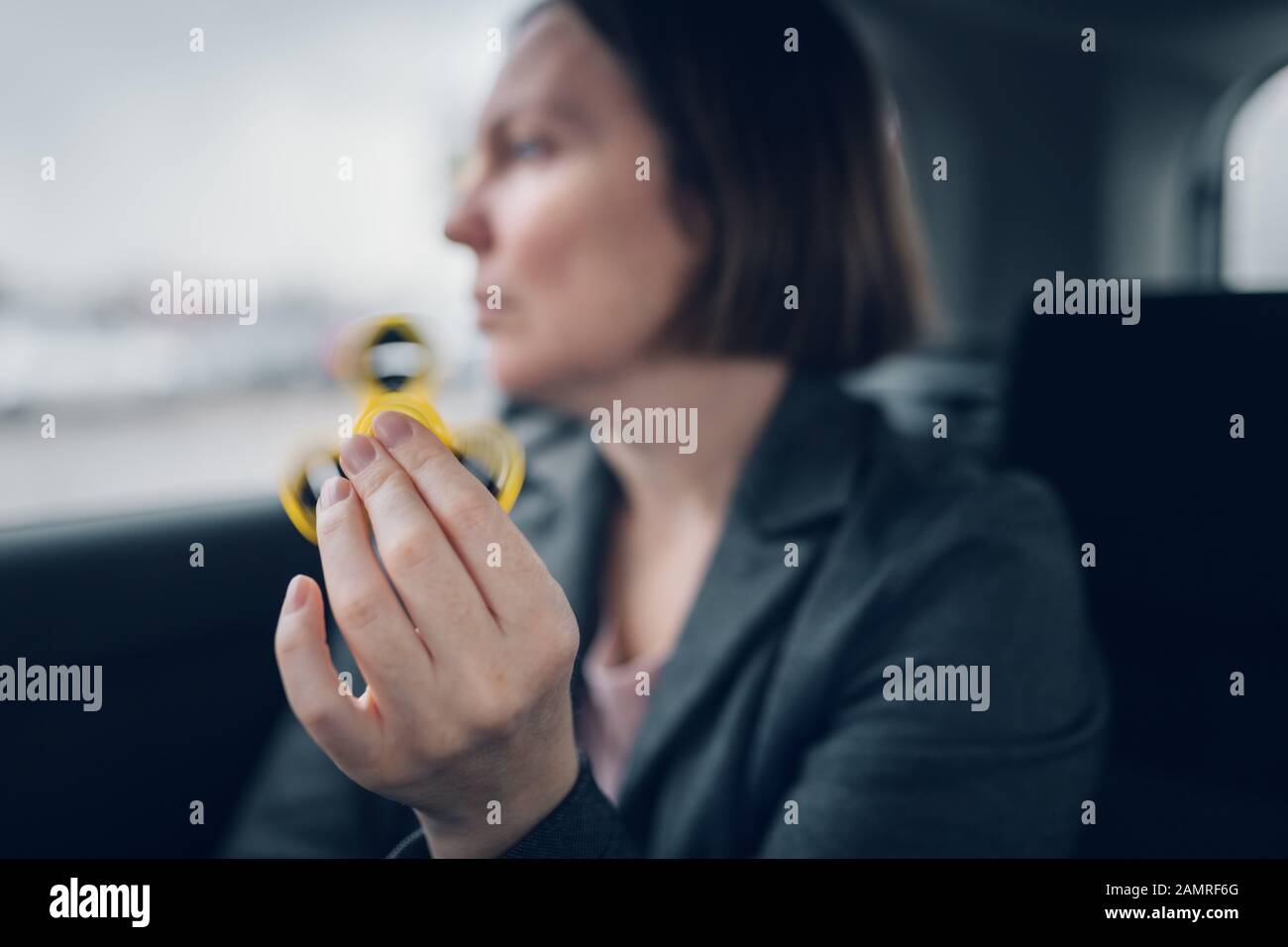 Businesswoman playing with fidget spinner in car while sitting at the backseat of the vehicle and commuting to work, selective focus Stock Photo