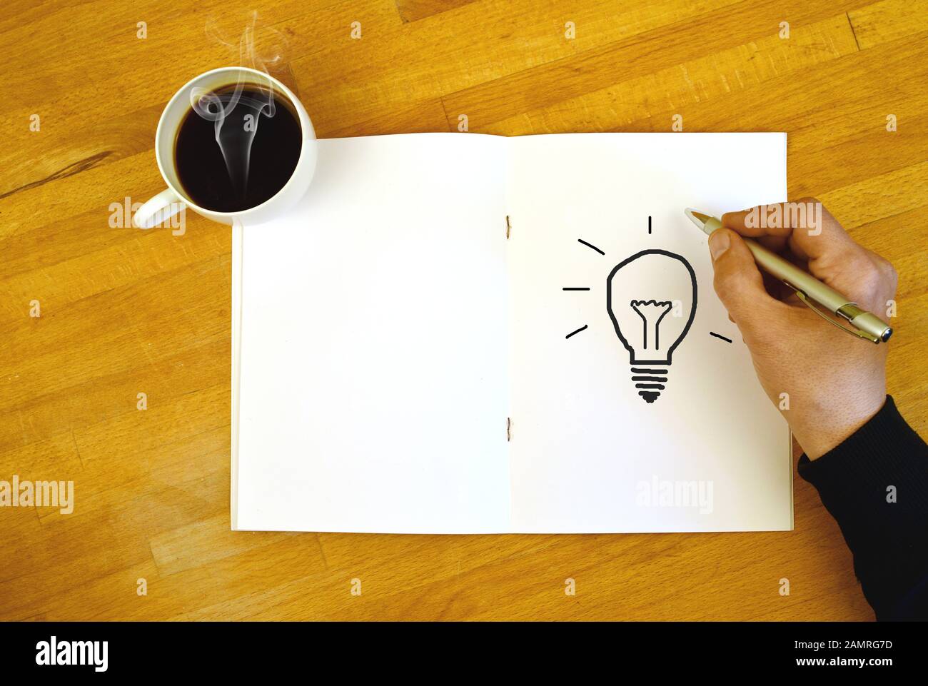 Brainstorming on a desk with paper and coffee, a hand drawing a lamp symbol Stock Photo