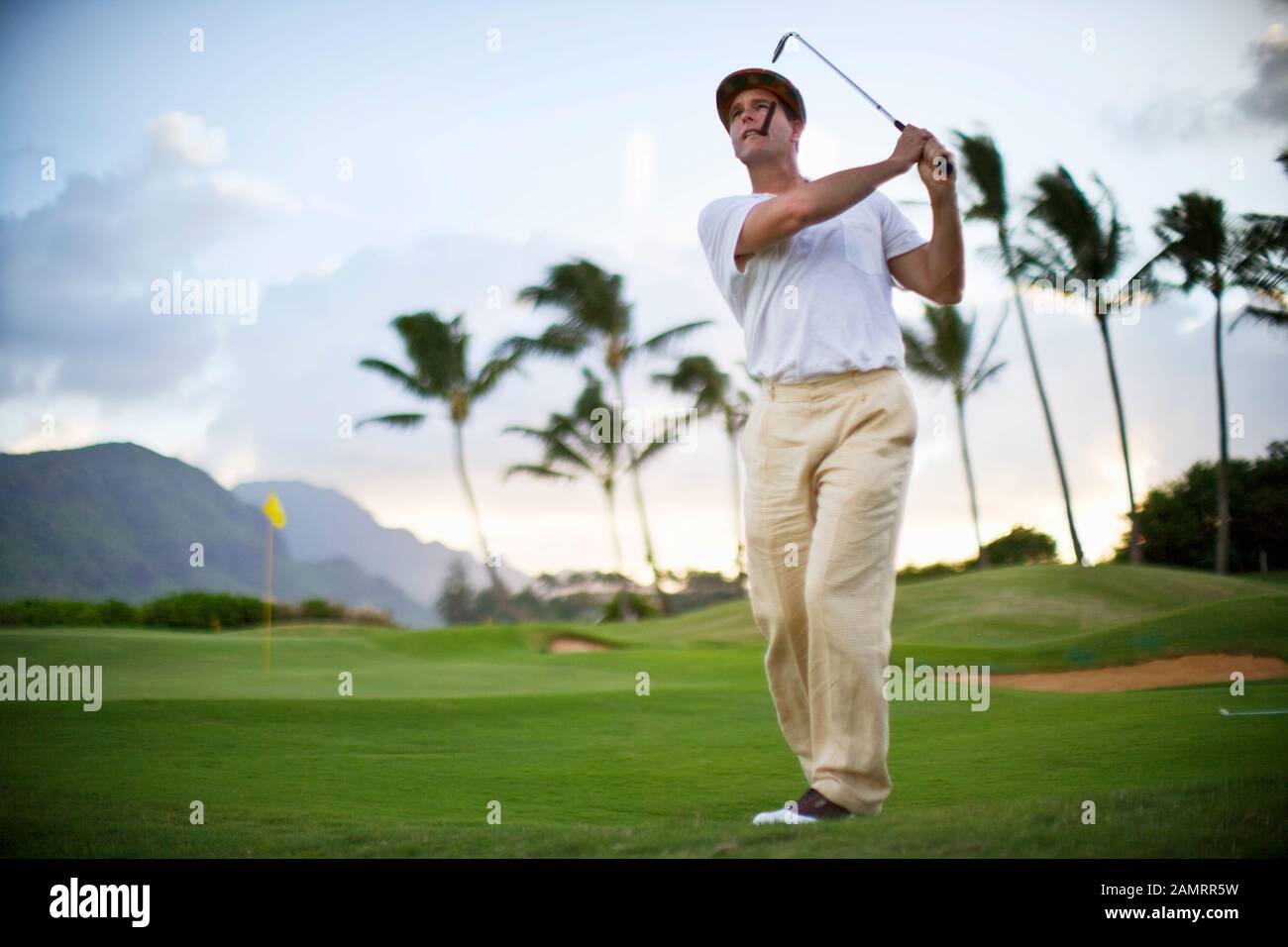 Male golfer smoking a cigar looks up as he stands with his arms raised