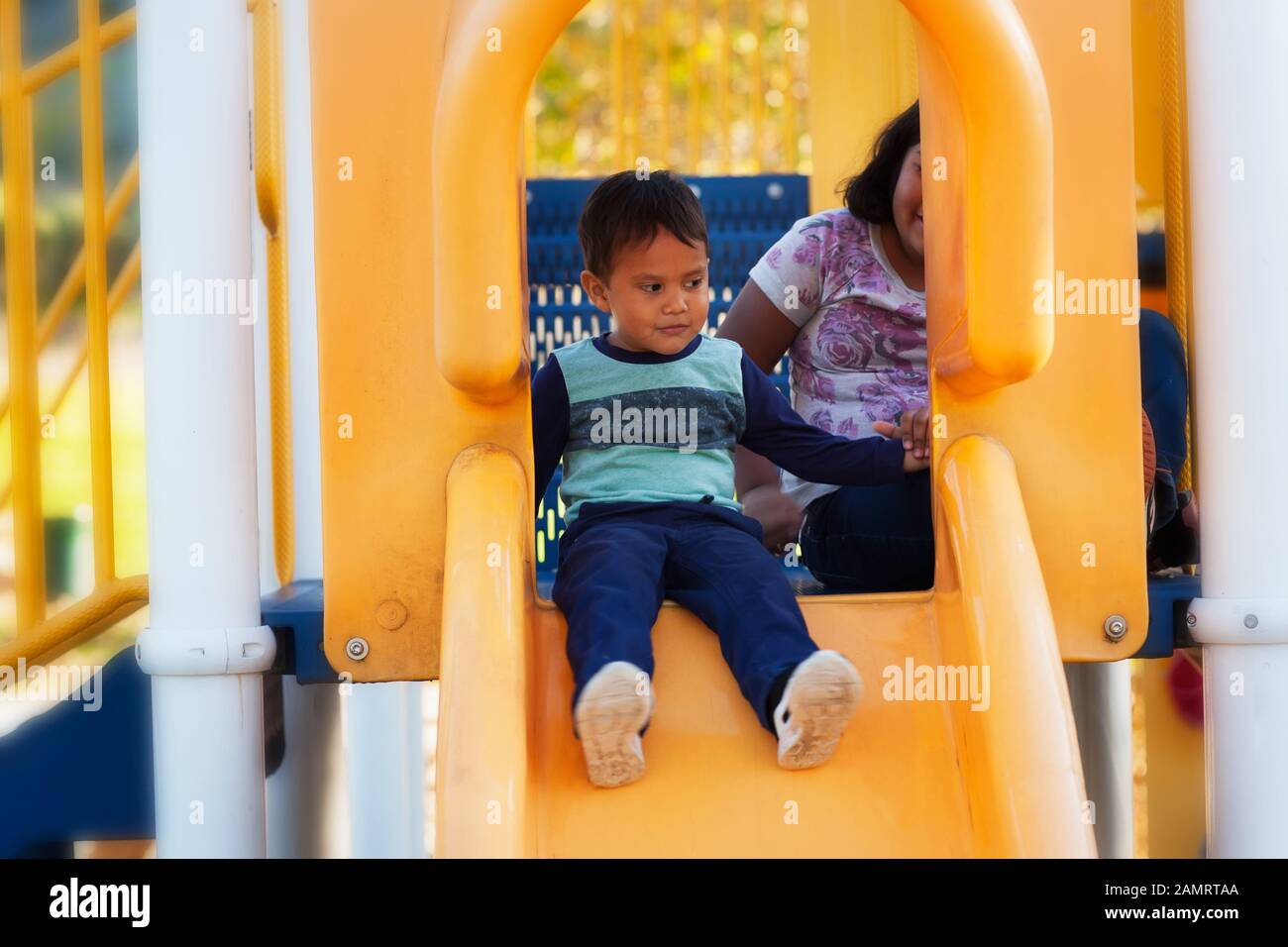 A little boy holding on to his big sisters hand before letting go on a kids playground slide. Stock Photo