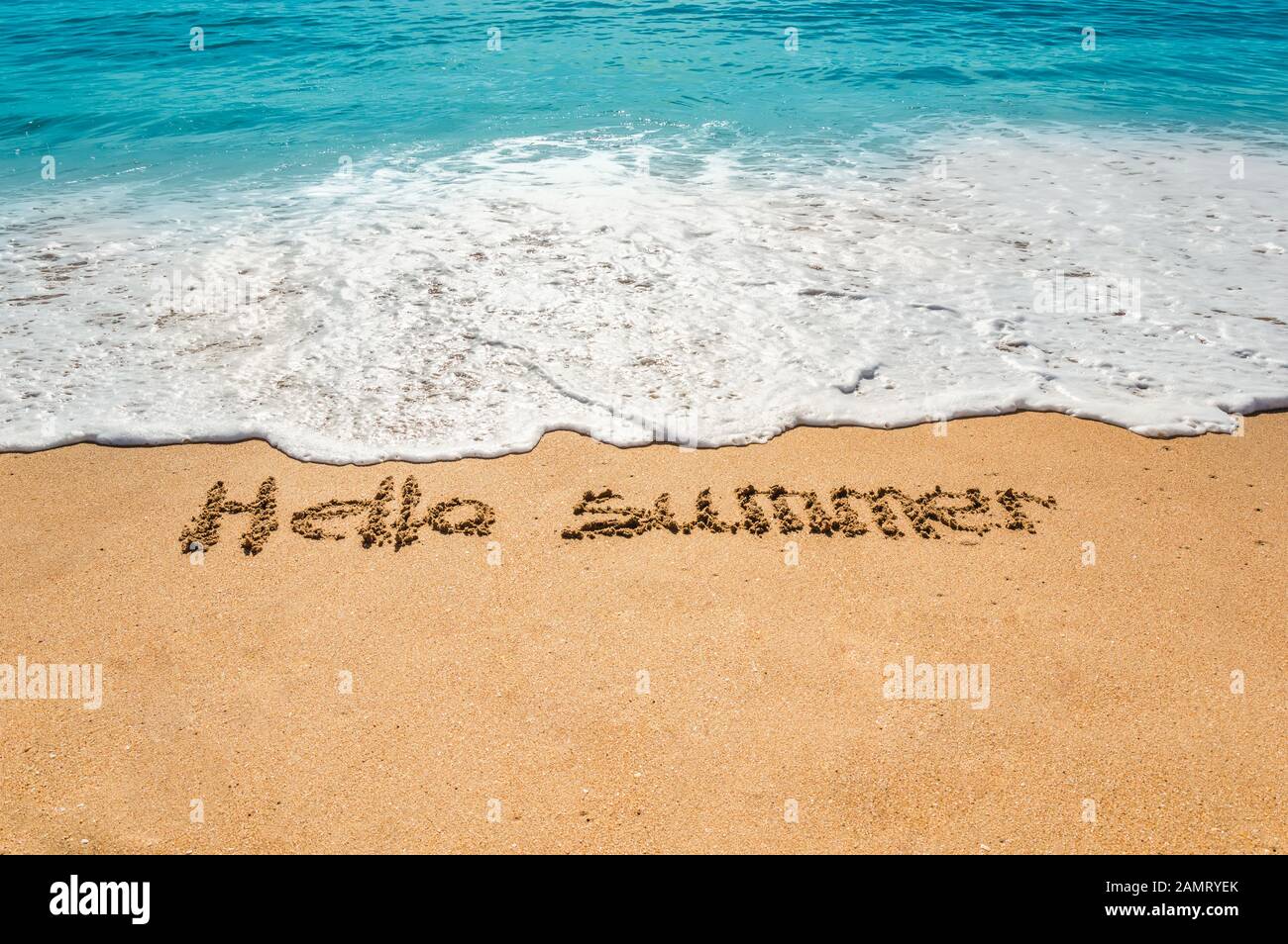 Hand written text hello summer on the golden beach sand with coming waves. Hot summer holidays and vacation at the sea. Relaxation concept. Stock Photo