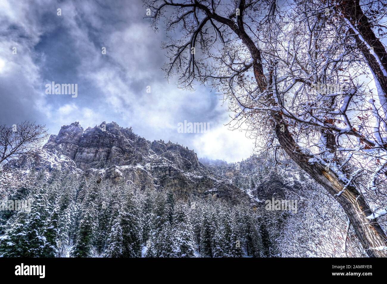 High altitude clouds swirl around the rugged peaks and snow dusted forests of the Wasatch Mountains in Utah. Stock Photo