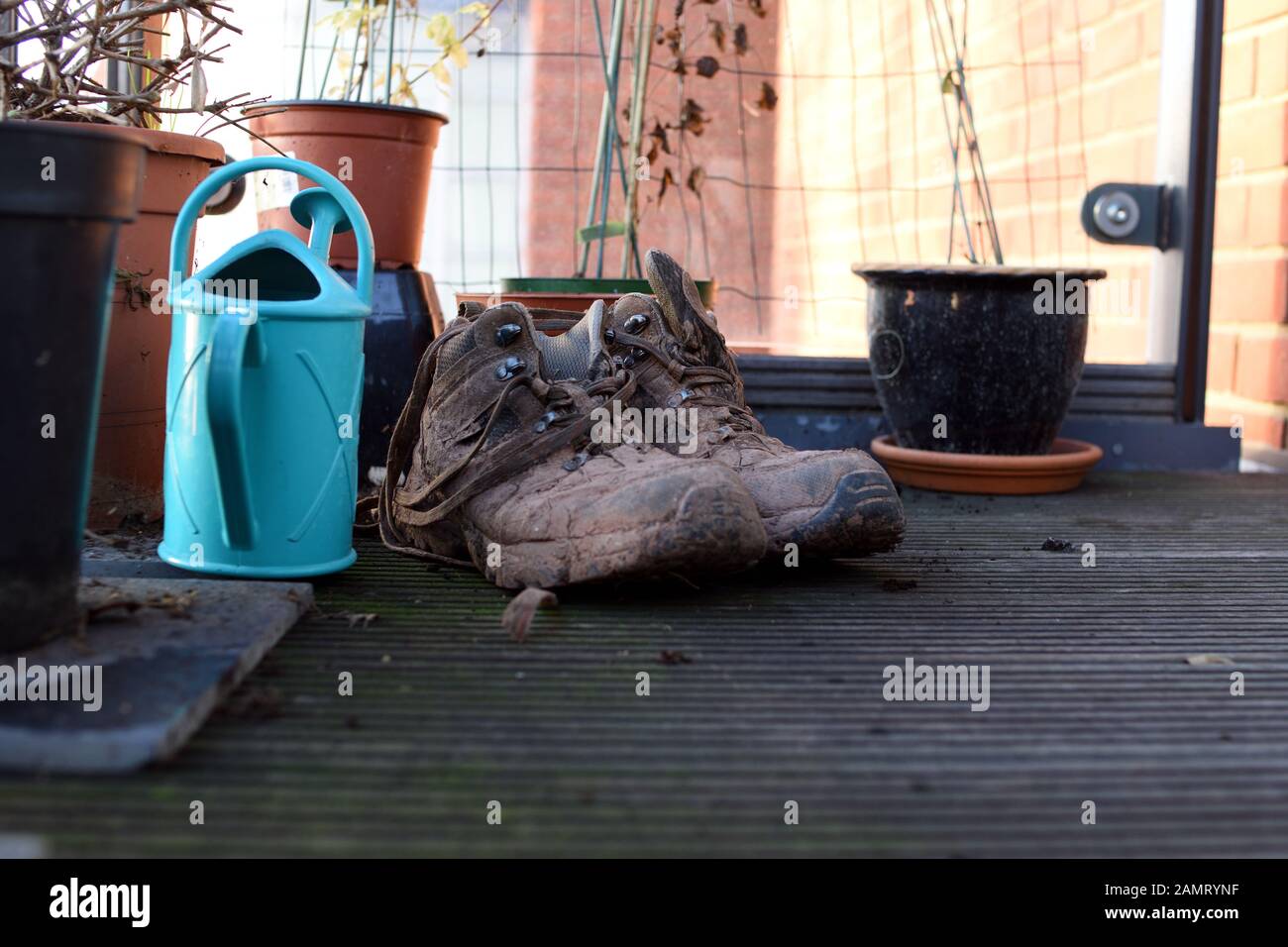 Muddy boots for gardening next to plastic turquoise watering can on a balcony Stock Photo