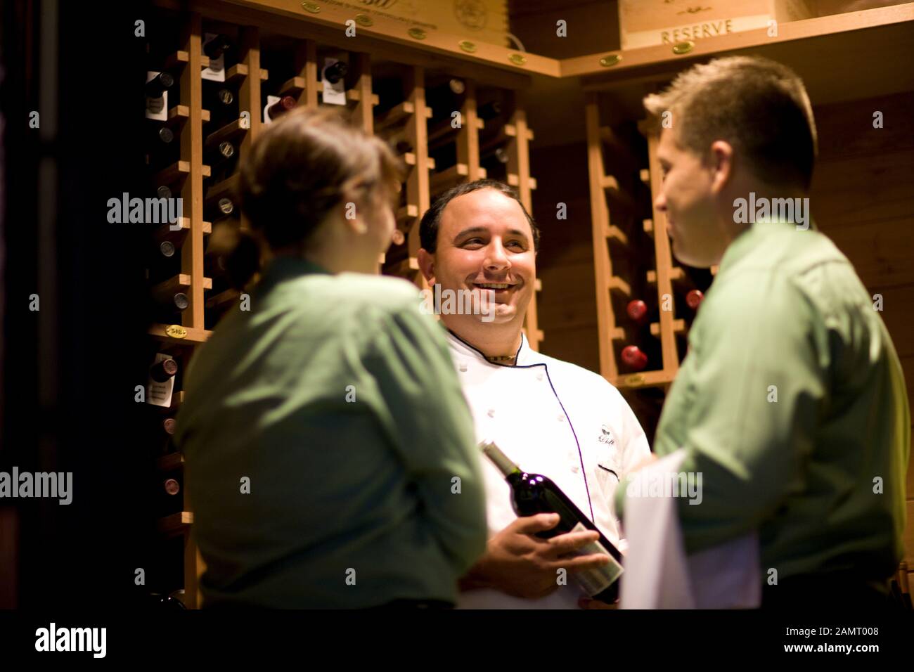Mid-adult male chef with two wait staff in a wine cellar. Stock Photo