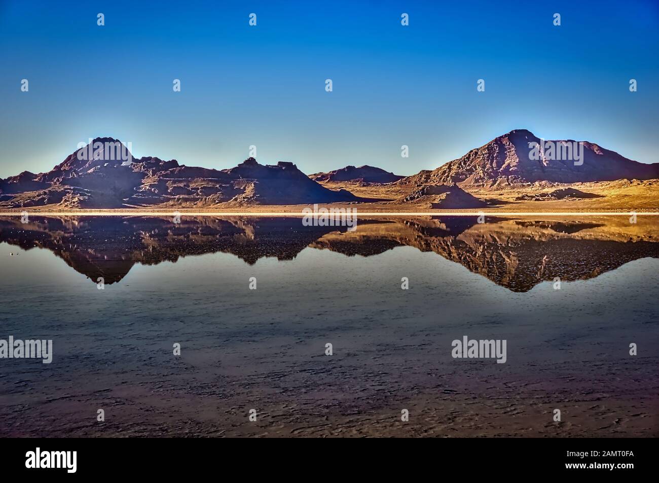 Rugged rocky mountains reflect on the smooth mirror-like waters covering the Bonneville Salt Flats in Western Utah in the United States. Stock Photo