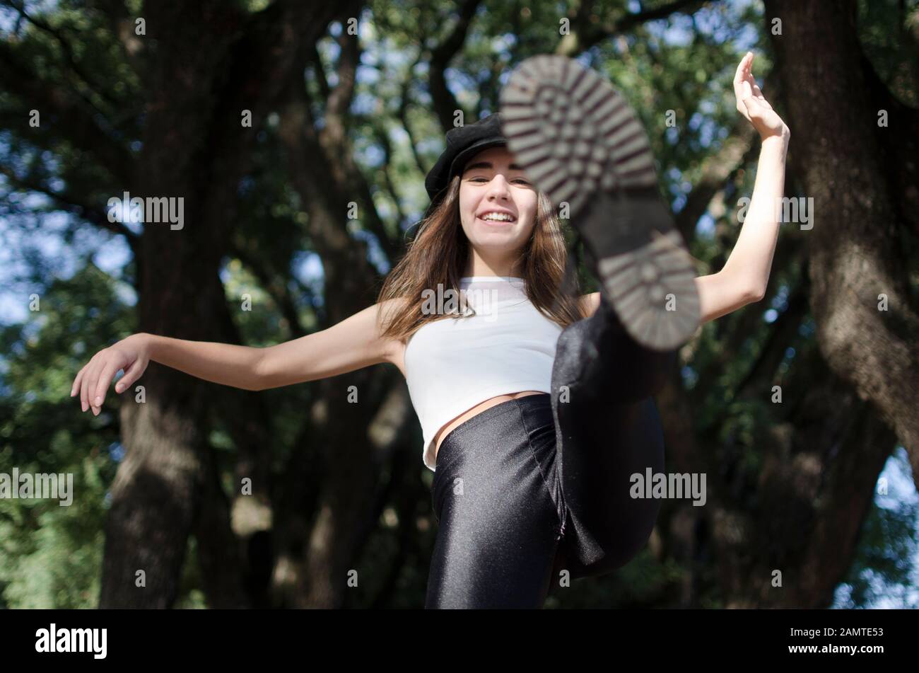 Smiling teenage girl standing in a park kicking her leg in the air, Argentina Stock Photo