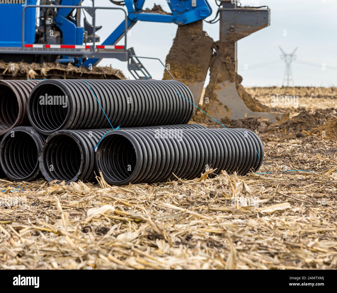 Black corrugated water drainage pipe, field tile, in farm field with tile plow or ditcher in background Stock Photo