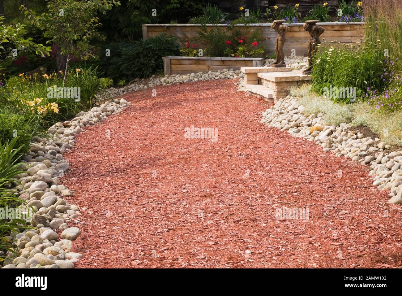 Rock edged red cedar mulch path and borders with yellow Hemerocallis - Daylily and white Leucanthemum vulgare - Oxeye Daisy flowers in backyard garden Stock Photo