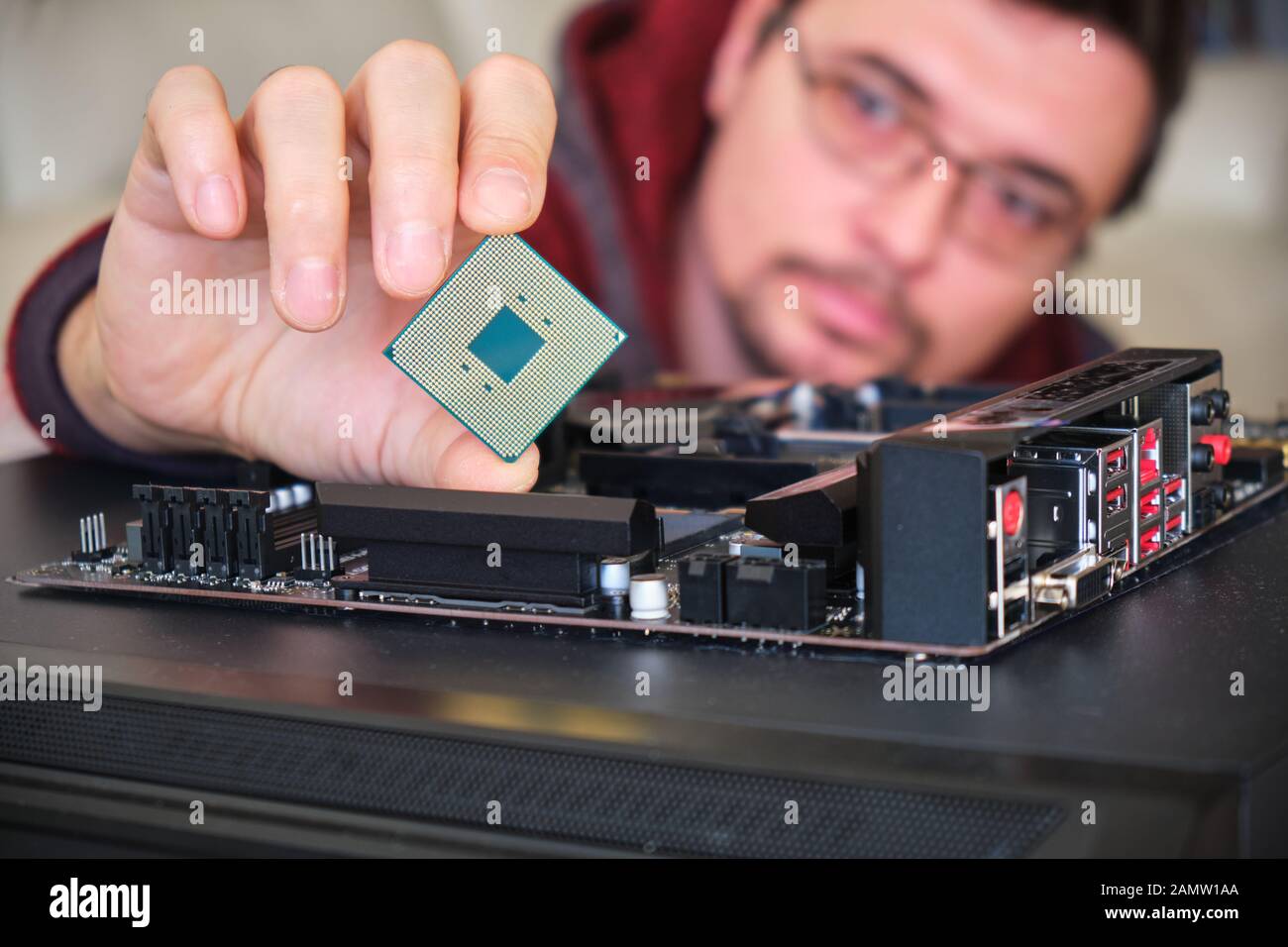 Man examining a computer chip held between his fingers, above a motherboard. Stock Photo