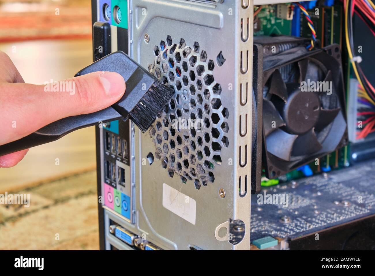 Cleaning dust from a cooler inside a computer case, using a small vacuum tube with a brush. PC maintenance concept. Stock Photo
