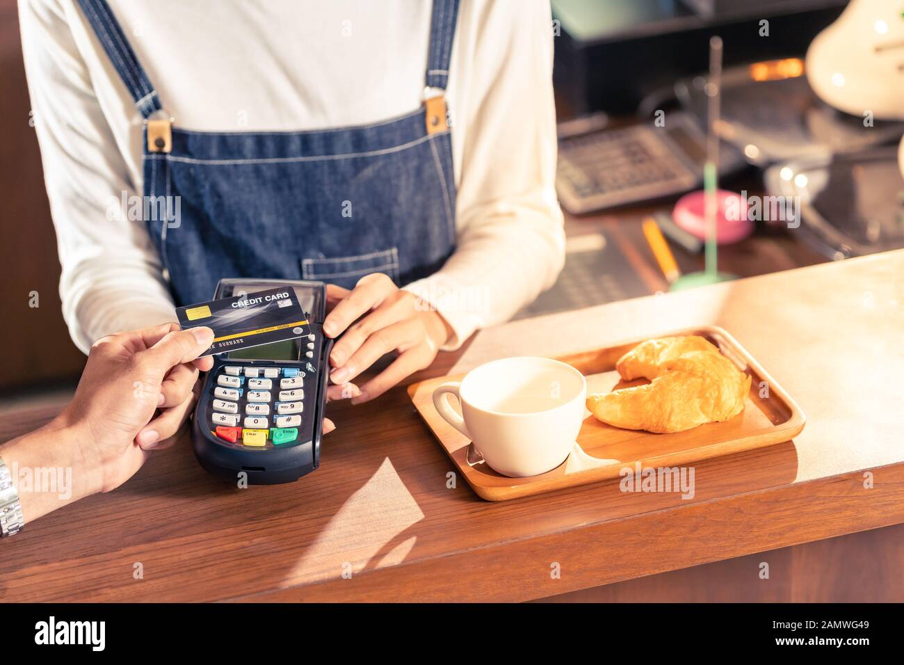 Close-up of asian customer using his credit card with contactless nfs technology to pay a barista for his coffee purchase at a cafe bar. Stock Photo