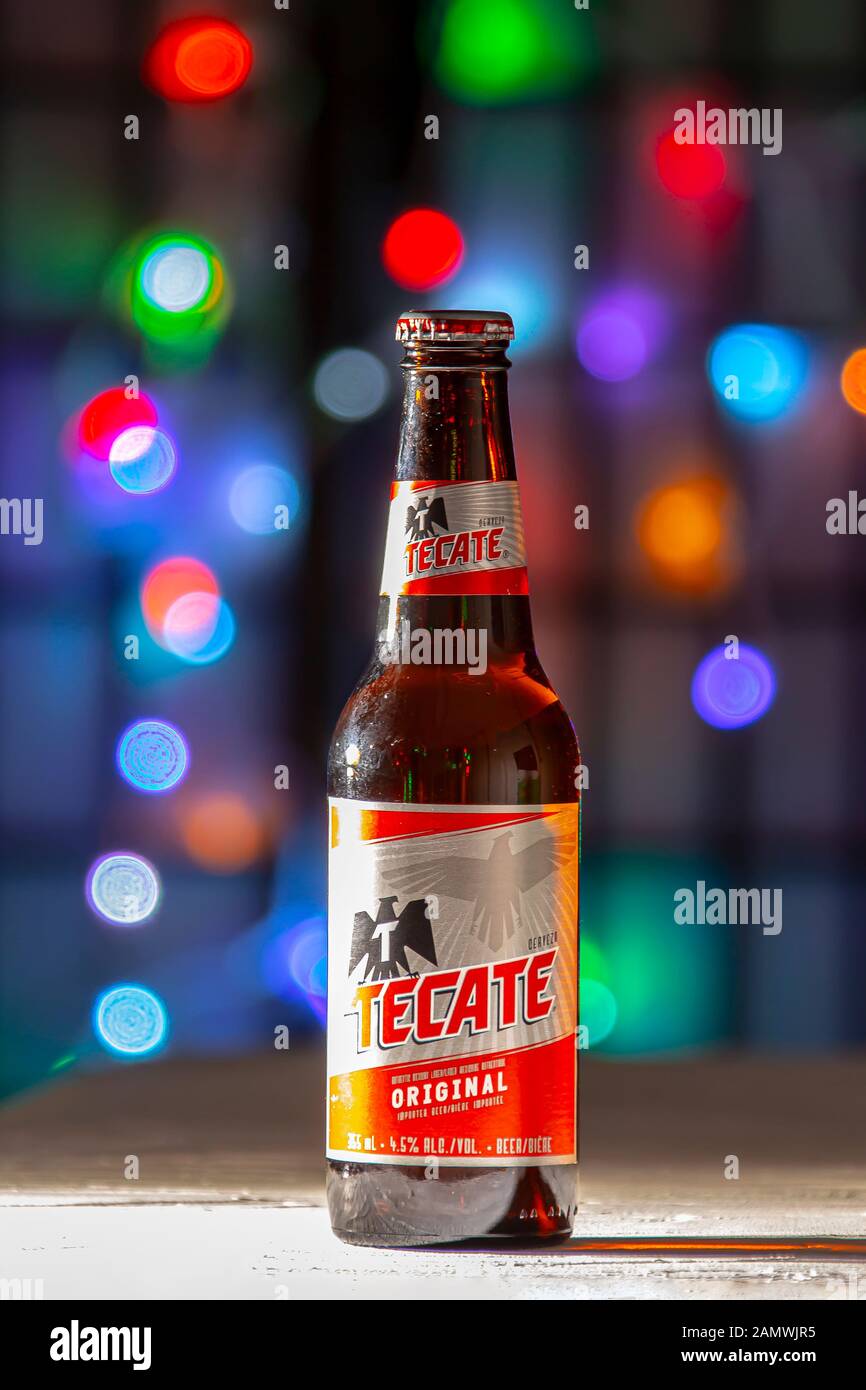 A Bottle of Tecate Beer. A mexican beer on a white texture surface on a colorful defocused lights Stock Photo