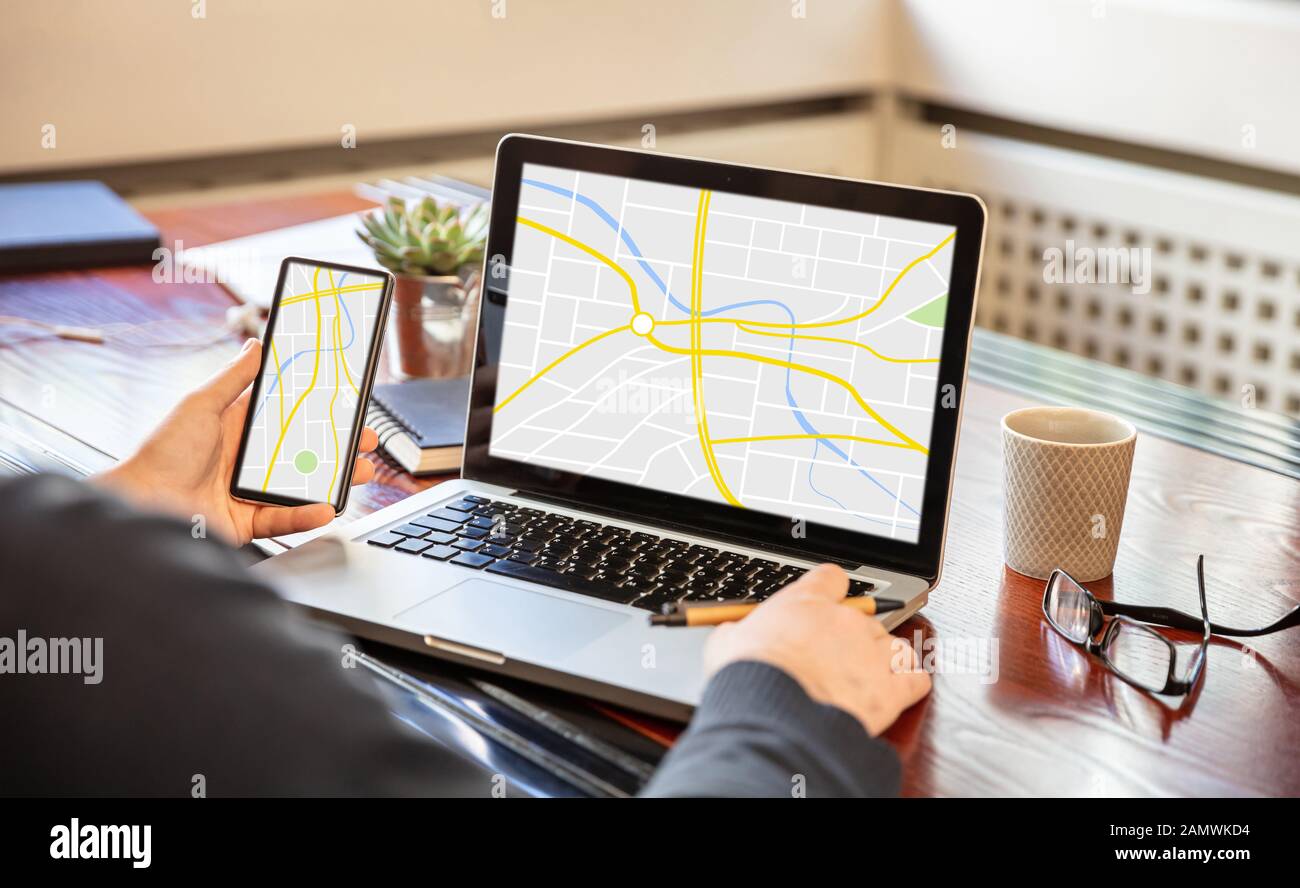Map online, GPS, navigation concept. Man holding a mobile phone and working with a computer, digital map on the screens, office business background. Stock Photo