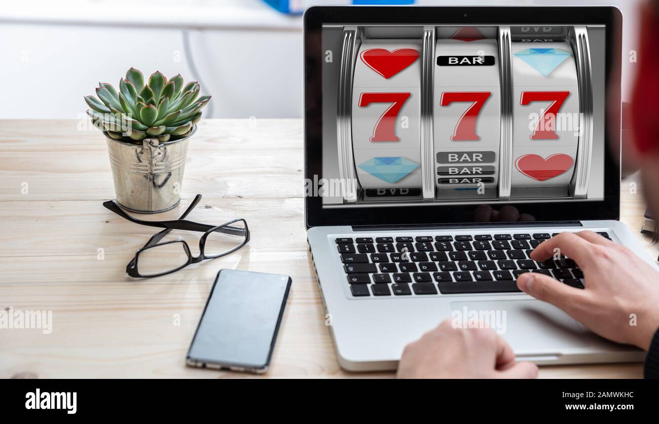 Slot machine, online casino gambling concept. Man working with a computer laptop, 777 on the screen, office business background. Stock Photo