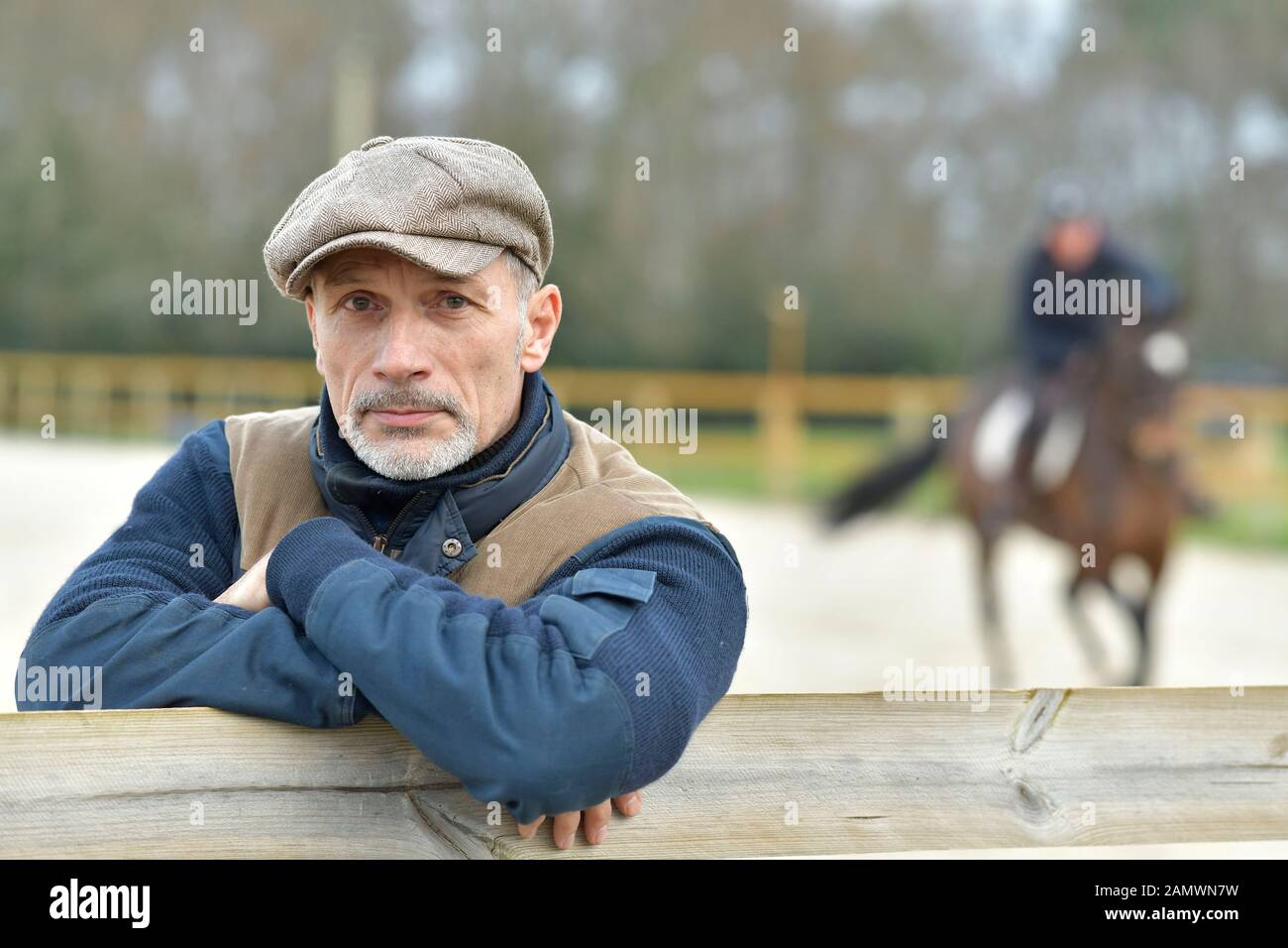 Portrait of horseman leaning on fence, horse in background Stock Photo