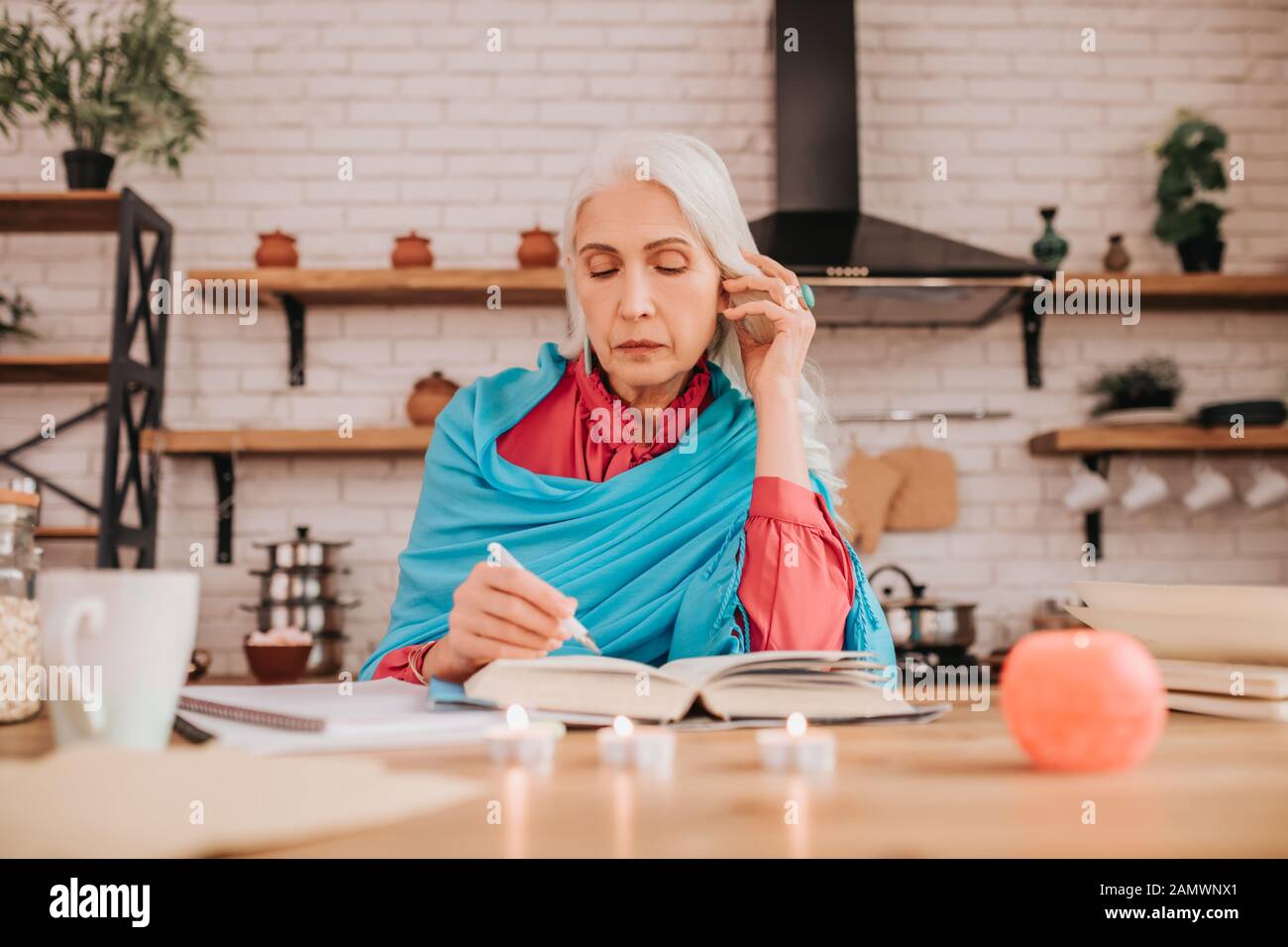 Grey-haired beautiful elderly lady in blue shawl making notes Stock Photo