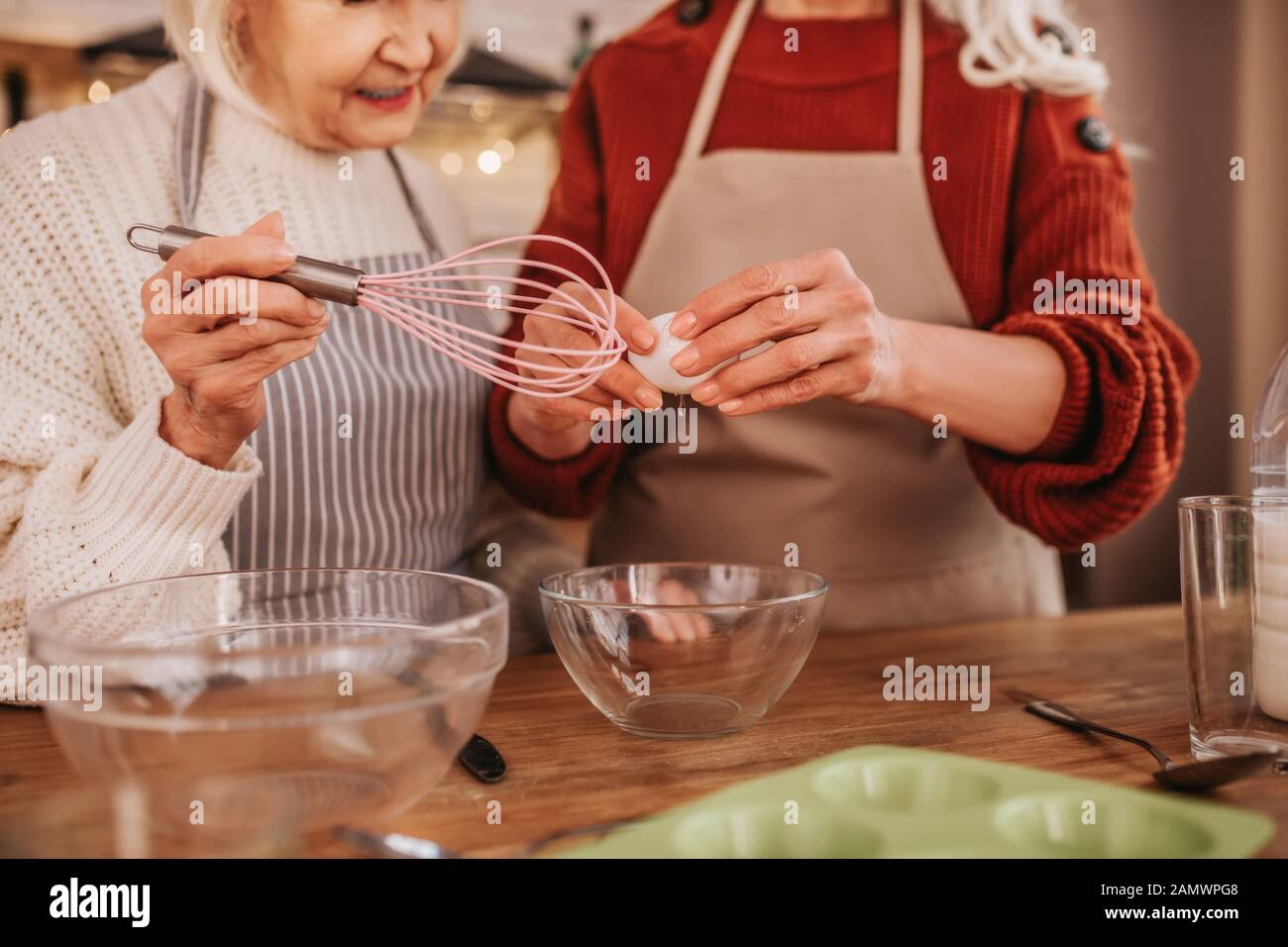 Grey-haired smiling ladies in aprons whipping milk Stock Photo