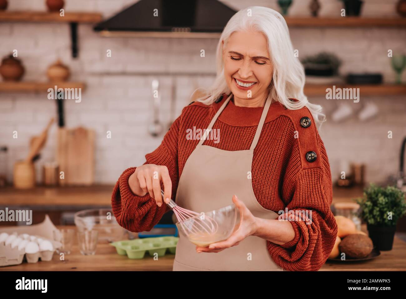 Grey-haired smiling lady whipping milk in a bowl Stock Photo