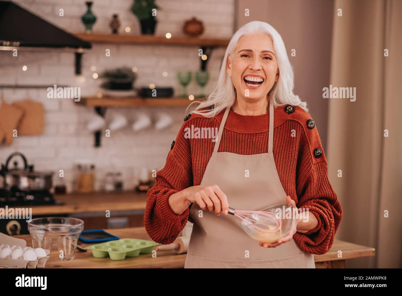 Grey-haired smiling lady smiling bright whipping milk in a bowl Stock Photo