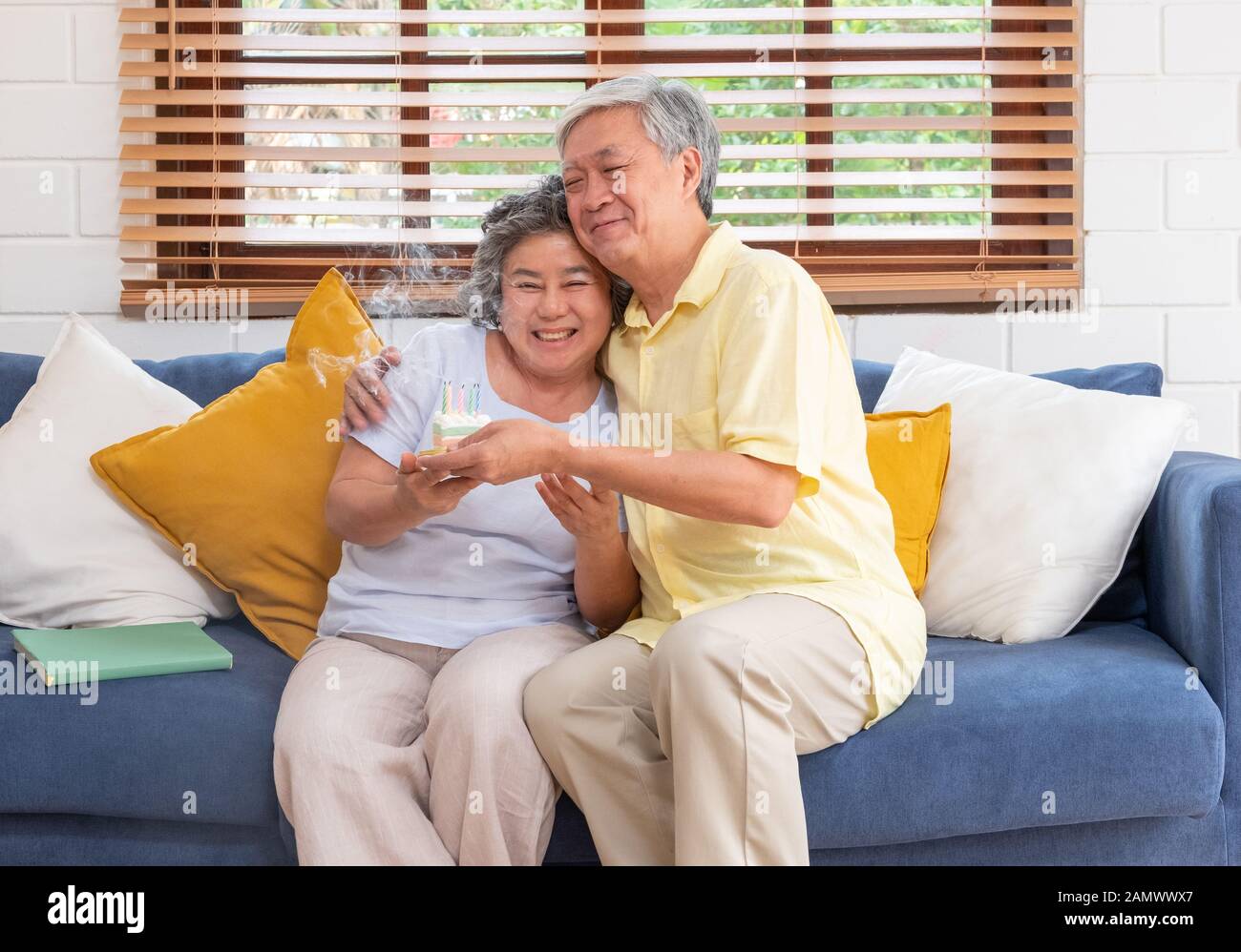 asian senior man surprise senior woman with birthday cake in living room at home.aging at home concept. Stock Photo