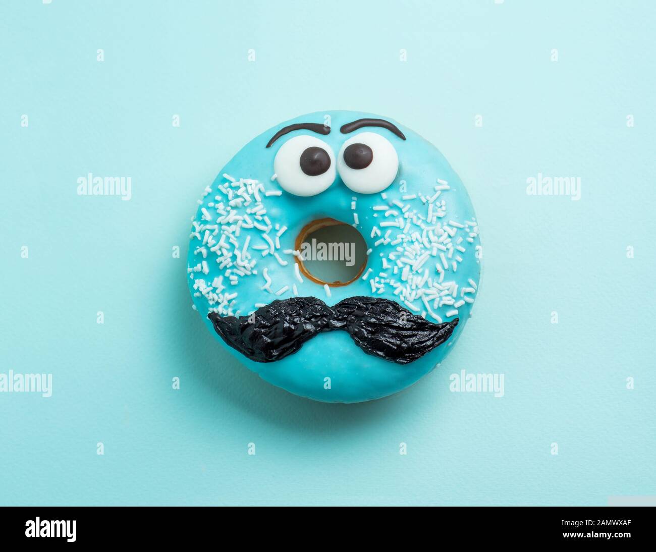 Blue glazed donut with mustache. Blue doughnut with funny face with mustache on blue background. Copy space for text. Masculinity or father day concept. Top view or flat lay Stock Photo