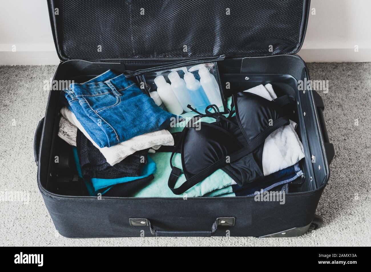travel essentials and packing for a holiday concept, luggage with pile of  clothes beach towel and bikini next to transparent liquid bag for airport  se Stock Photo - Alamy