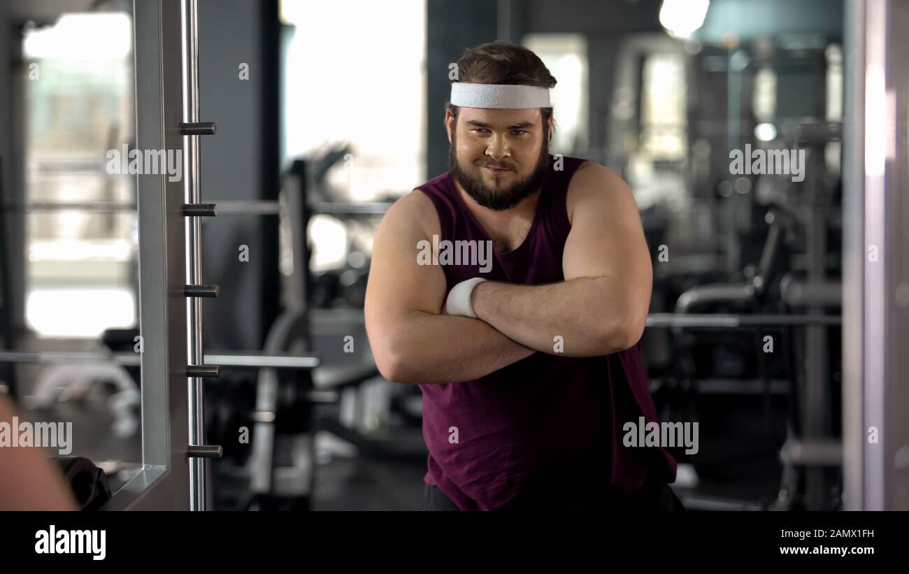 Fat man with folded hands looking at mirror, satisfied with weight loss