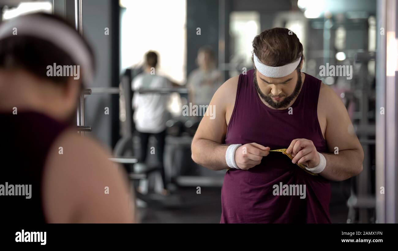 Overweight man measuring fat waist, checking result after dieting and