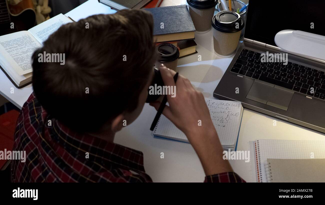 Schoolboy drinking coffee while preparing for exam at night, doing homework Stock Photo
