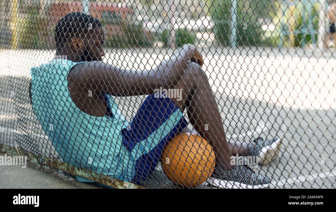 Tired African-American basketball player relaxing after game at stadium, hobby Stock Photo