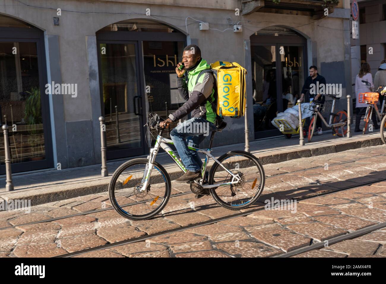 Milan, Italy - January 11, 2020: A Glovo rider cycles on a city centre street. Food delivery service. Online ordering. Stock Photo