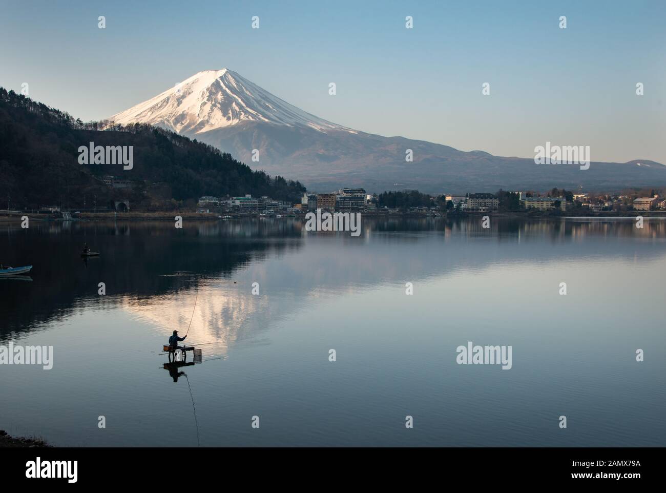 View of Mount Fuji reflected in the lake Kawaguchiko with fishermen out fishing on the lake Stock Photo