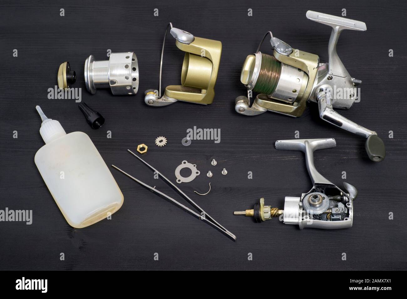A fishing spinning reel as a whole and a second similar completely  disassembled. The main parts ready for lubrication and the tweezers in the  foregrou Stock Photo - Alamy